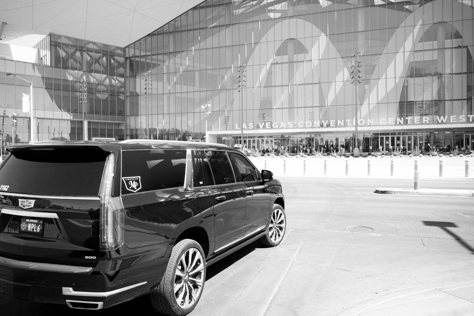 Black-and-white photo of a black Cadillac Escalade with MP Limousine branding parked in front of the glass facade of the Las Vegas Convention Center West building.