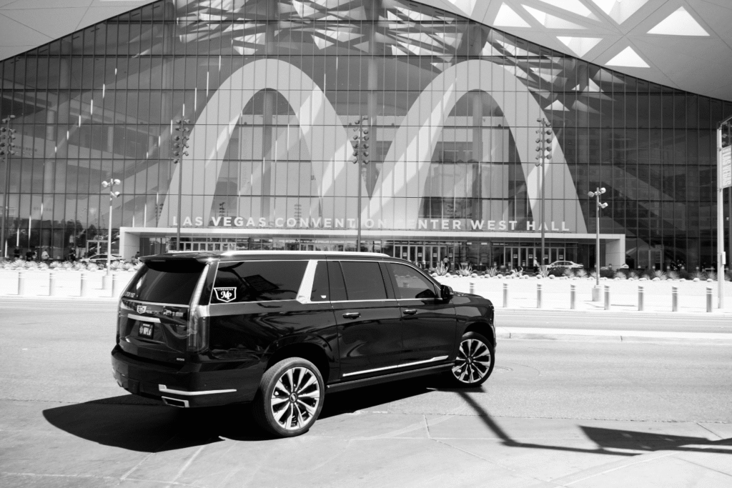 Black-and-white photo of a black Cadillac Escalade with MP Limousine branding parked in front of the curved glass facade of the Las Vegas Convention Center West Hall.