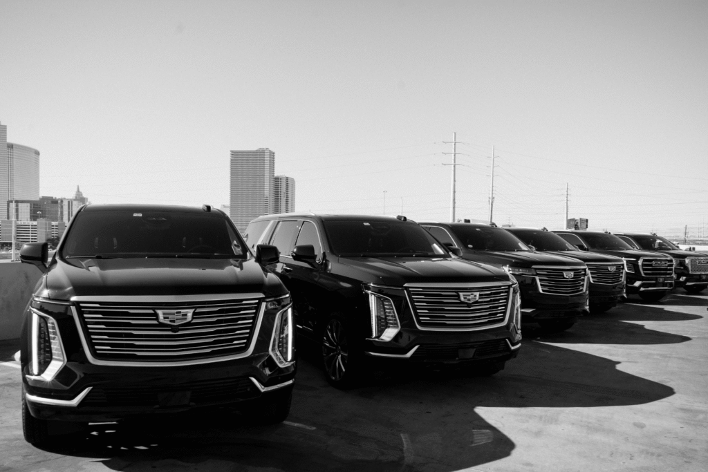 Black-and-white photo of a row of black Cadillac Escalade and GMC SUVs parked in formation on a rooftop lot, with the Las Vegas skyline in the background.