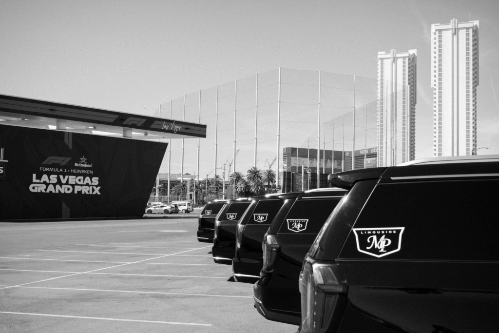 Black-and-white photo of a row of black SUVs with MP Limousine logos on their rear windows lined up beside the Formula 1 Heineken Las Vegas Grand Prix entrance, with high-rise towers in the background.