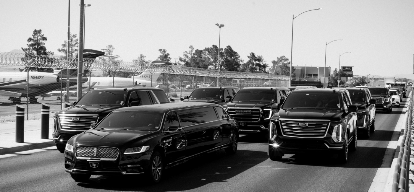 Black-and-white photo of the MP Limousine fleet—a black stretch limousine, Cadillac Escalades, and GMC SUVs—staged together on a roadway beside a private airfield with parked jets in the background.